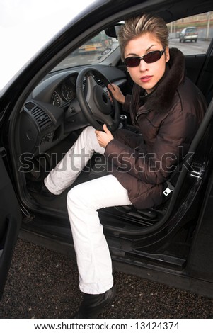 pretty woman with sun glasses stepping out of her car hands on the wheel, looking at left side