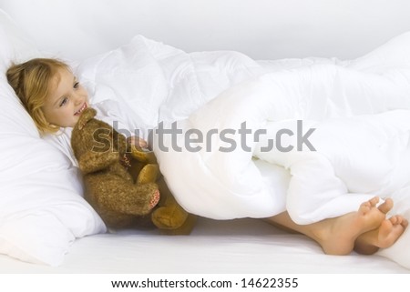 Little blond girl wearing white blouse in white bedchlothes