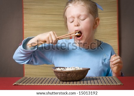 Little girl in blue eating rice with chopsticks