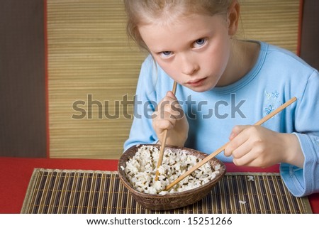 Little girl in blue eating rice with chopsticks