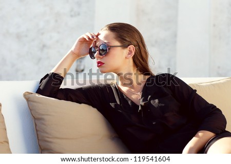 young beautiful woman in black clothes sitting on sofa outdoors in summer