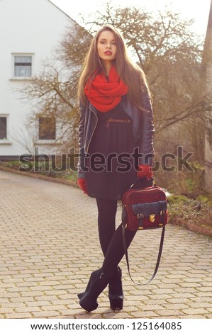 fashionable stylish girl in black dress and leather jacket with red bag