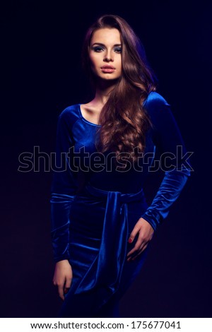 Elegant lady posing against black background. Young beautiful woman wearing blue dress fashion style portrait.