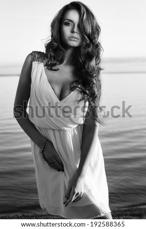 elegant sexy lady. beautiful stunning girl in white dress posing at sea coast against blue sky at sunset