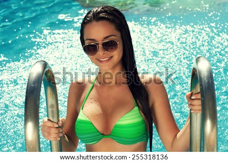 POrtrait of young sexy tanned girl posing in swimming pool in green bikini on a summer day