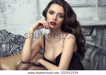 Fashion portrait of young beautiful sexy woman with long wavy hair. Pretty girl sitting in black bra or lingerie in luxury interior and looking at you.