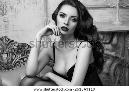 Fashion portrait of young beautiful sexy woman with long wavy hair. Pretty girl sitting in black bra or lingerie in luxury interior. Monochrome colors portrait