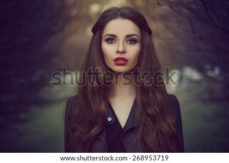 Art portrait of beautiful lonely girl. Pretty woman with long dark hair and red lips posing in forest and looking at you. Shallow DOF