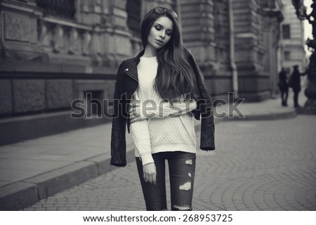 Fashion style portrait of young beautiful calm female model posing at city street with magnificent architecture. Monochrome portrait.
