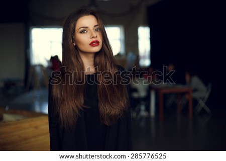 Natural light indoor portrait of young pretty girl with long dark brown hair, natural makeup and red lips. Stylish woman looking at you