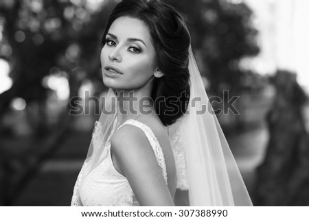 Wedding. Closeup portrait of young beautiful bride in white dress and veil looking at you. Black and white photo