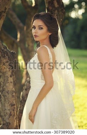 Wedding. Young beautiful bride in white dress standing near tree in park. Full body portrait. Soft sunset lovely lightning