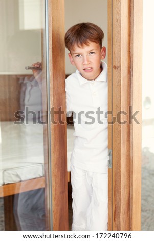 Surprised boy peeks from behind door, indoor