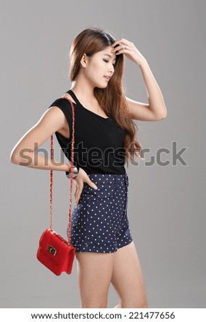 Asian woman posing in a black vest top and polka-dot shorts with red sling bag and bracelet in studio.