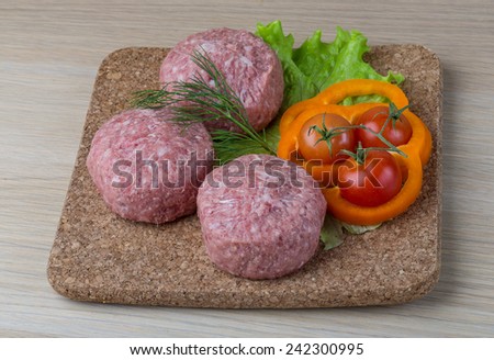 Raw burger cutlet with salad leaves on the wooden background