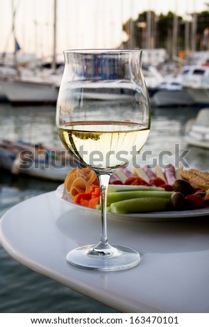 Wineglass with white wine and variety of food with background sea and boats