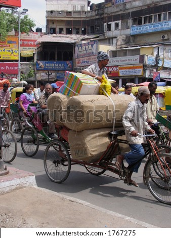 A man rides a heavily-laden rickshaw through the chaotic streets of Old Delhi, India