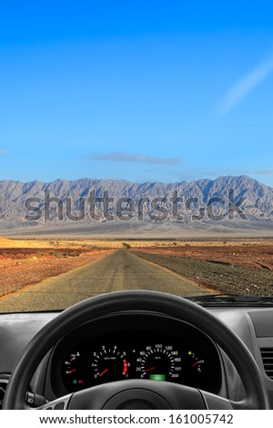 Wheel and dashboard of the car going on the desert road to far mountains