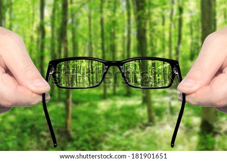 Hands holding and offering eye glasses to look at amazing green forest landndscape.Sharp as a good sight symbol and unsharp as a bad sight symbol