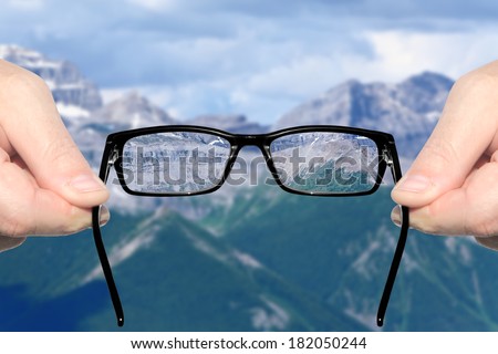 Hands holding and offering eye glasses to look at amazing mountain landscape. Sharp as a good sight symbol and unsharp as a bad sight symbol