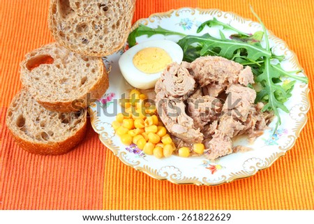 Canned tuna, sweet corn, boiled egg, sliced rye bread with bran and fresh salad leaves (rucola) on a bright color napkin.