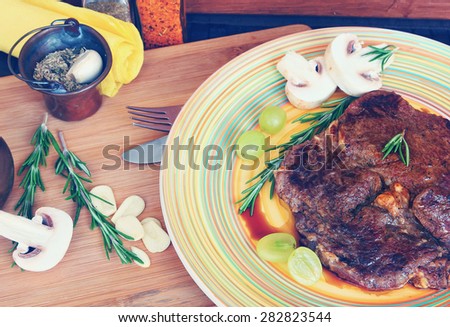 Meat (low fat beef steak) with fresh mushrooms, herbs and grapes of Mediterranean cuisine. Selective focus. Image done in vintage retro instagram style