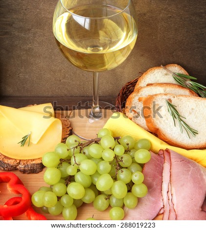 Glass of wine, grapes, cheese, meat and bread on wood background. Mediterranean snacks (food)