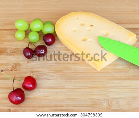Cheese and berry fruits ( sweet cherry and grapes) on the wood cutting board. Healthy food for breakfast or snack