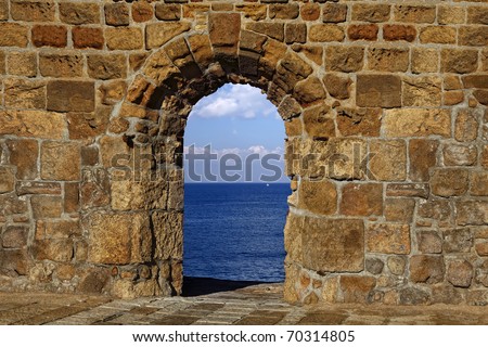 View on a lonely white sail in the dark blue sea through a window in an old fortification