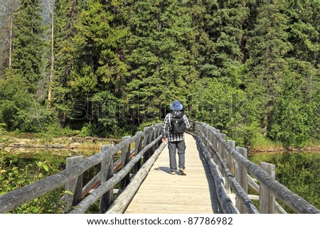 Man going on the wooden bridge through the river in a direction of wood