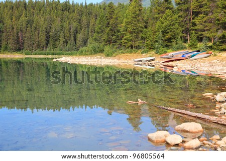View on the mountain lake with a smooth water and  tourist kayaks on the shore. Jasper National Park. Alberta, Canada