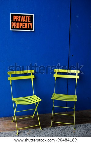 A private property sign over two chairs against a blue painted wooden wall