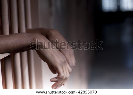 An African American man with hands outside the bars of a prison cell