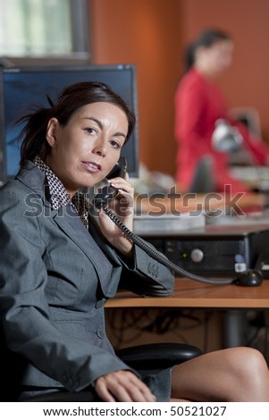 Businesswoman wearing a suit is having a conversation on the telephone in an office environment. Horizontal shot