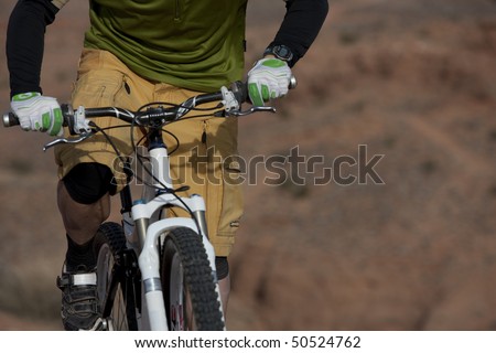 The torso of a man riding a mountain bike in a desert landscape. Horizontal shot.