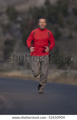 A man wearing athletic clothing is jogging down a road with a high desert landscape in the background. Vertical shot.