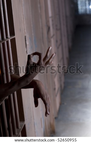 A man gestures the OK sign while sticking his hands through the bars of his prison cell. Vertical shot.