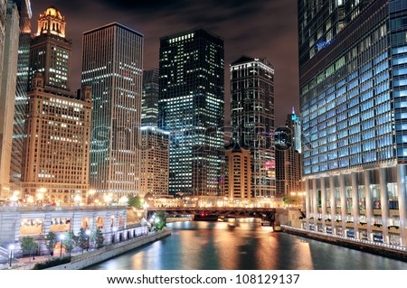 Chicago River Walk with urban skyscrapers illuminated with lights and water reflection at night.