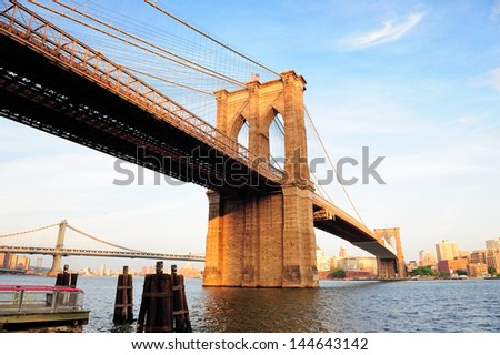 Brooklyn Bridge over East River viewed from New York City Lower Manhattan waterfront at sunset.