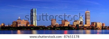 Boston city skyline with Prudential Tower and Hancock Building and urban skyscrapers over Charles River at dusk with lights and water reflection.