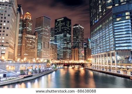 Chicago River Walk with urban skyscrapers illuminated with lights and water reflection at night.