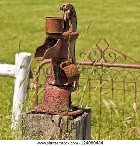 An old rusty water pump with its own rusty tin mug.