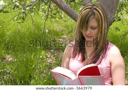 Young woman reading a book underneath an apple tree.