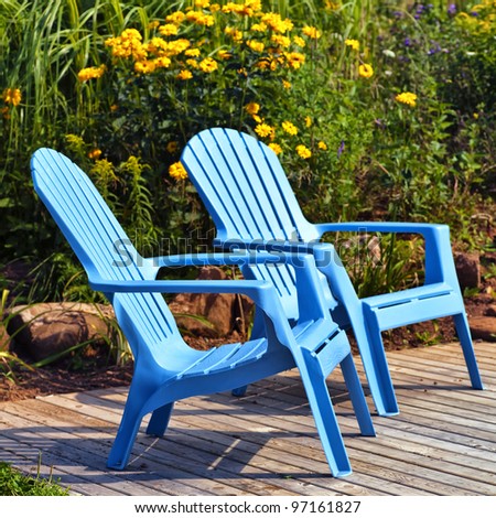 Brilliant blue plastic outdoor Adirondack chairs on the deck in a summer garden.