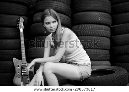 Young girl musician with electric guitar sitting on car tires. Black and white photo.