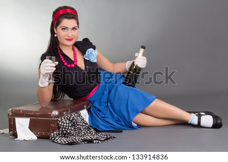 pinup girl with bottle of champagne and packed suitcase over grey