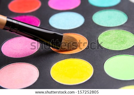 Make-up brush and eyeshadow palette over black close up