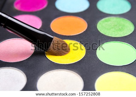 Make-up brush and colorful eyeshadow palette over black background close up
