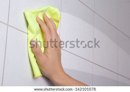 male hand with yellow rag cleaning the bathroom tiles
