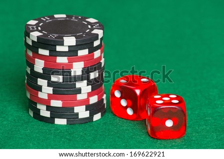 red and black poker chips and red dice on a green casino felt